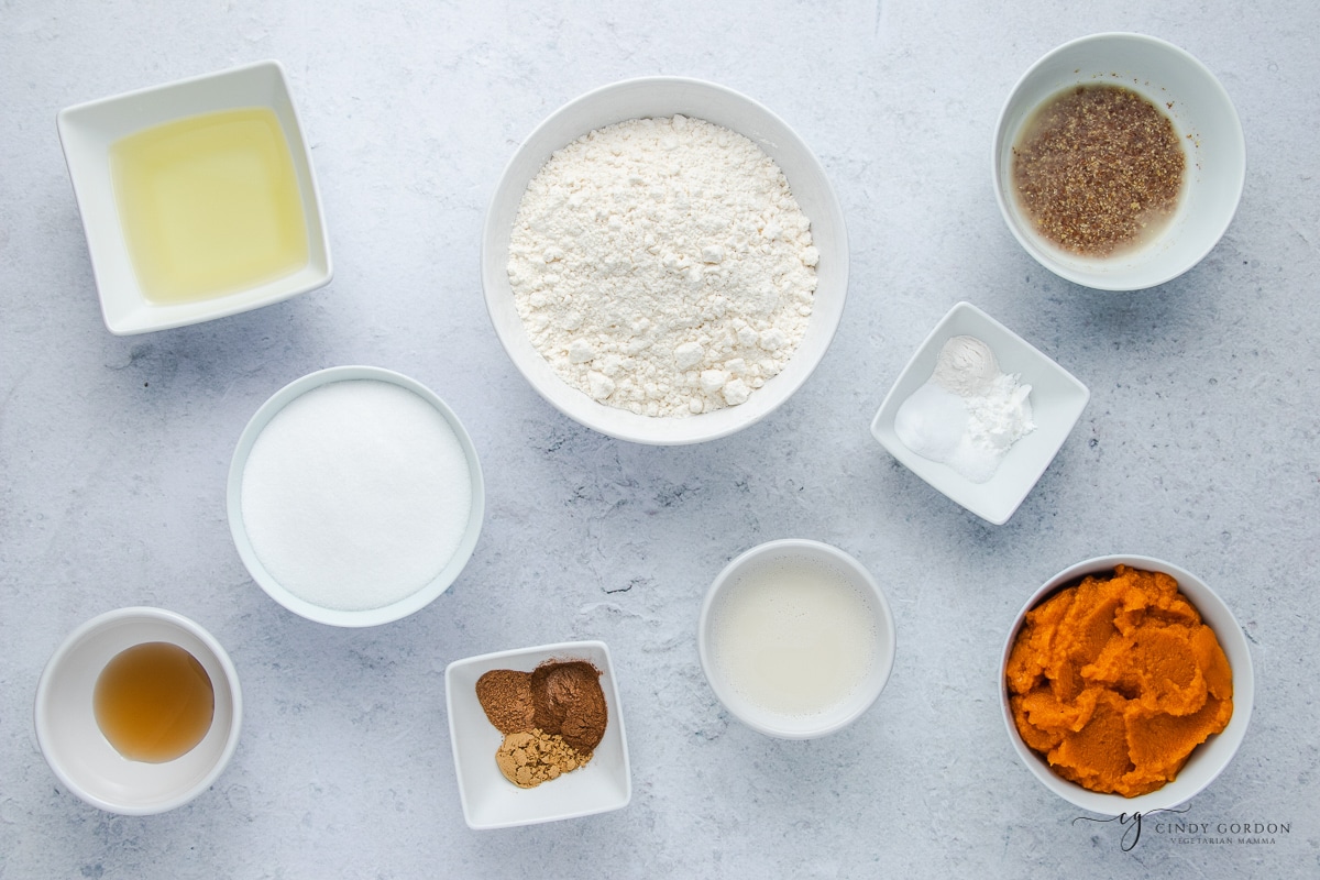 Bowls of gluten-free flour, pumpkin puree, flax egg, almond milk, vanilla extract, and spices