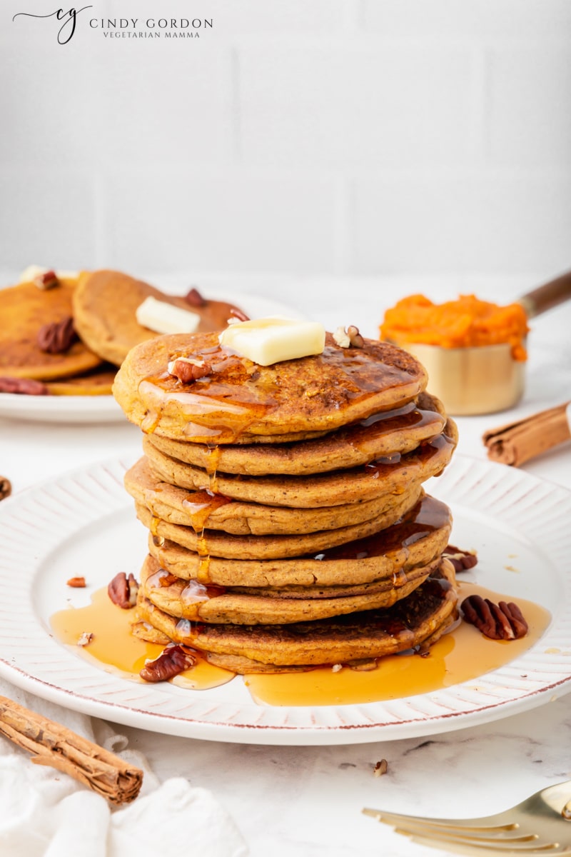 A tall stack of pumpkin pancakes covered with maple syrup and topped with vegan butter