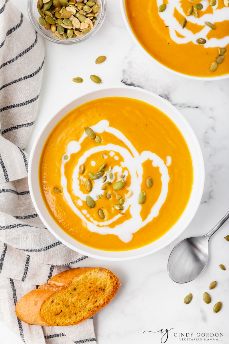 2 bowls of vegan pumpkin soup garnished with coconut milk and pumpkin seeds