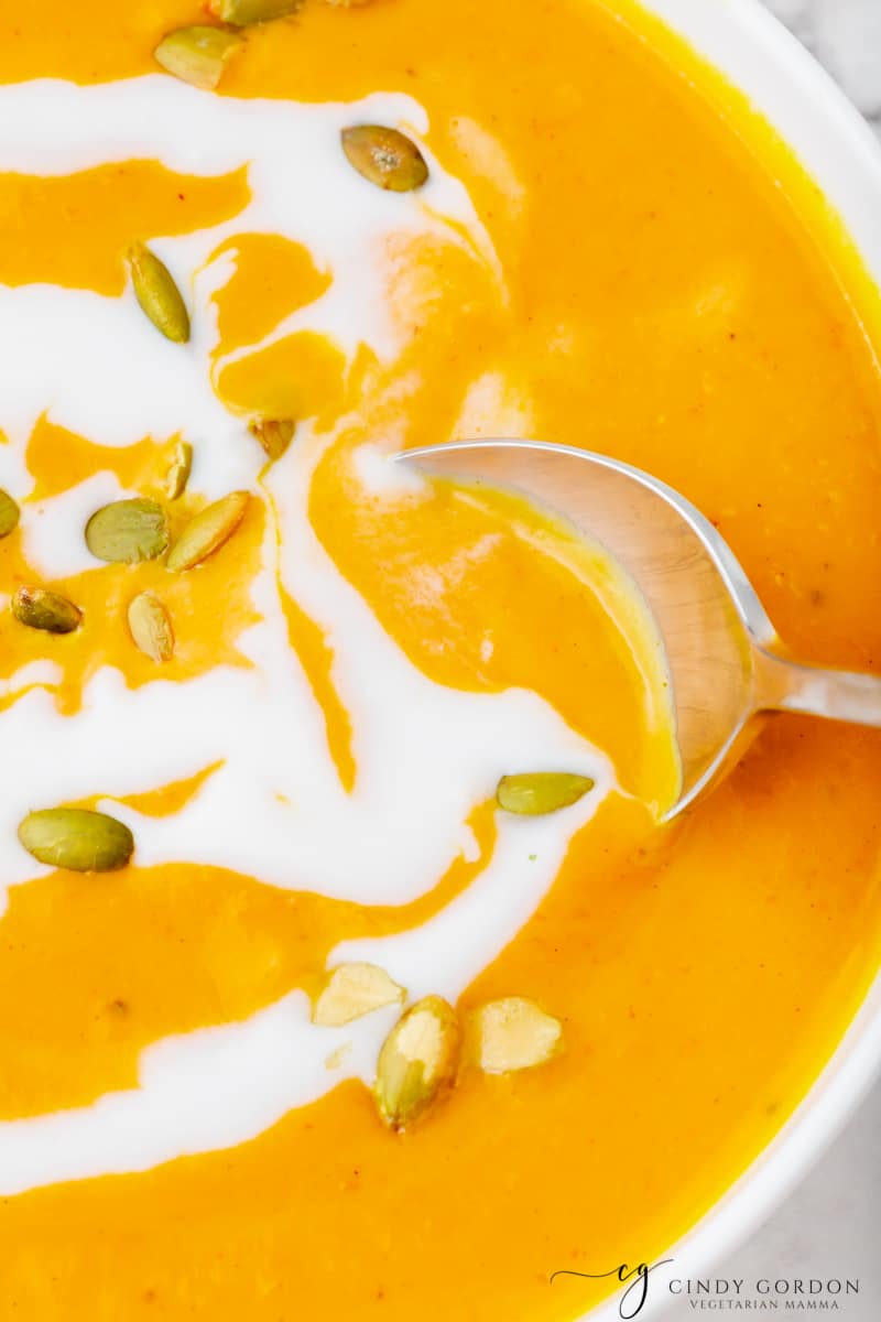 Close-up shot of a silver spoon in a bowl of pumpkin soup with coconut milk