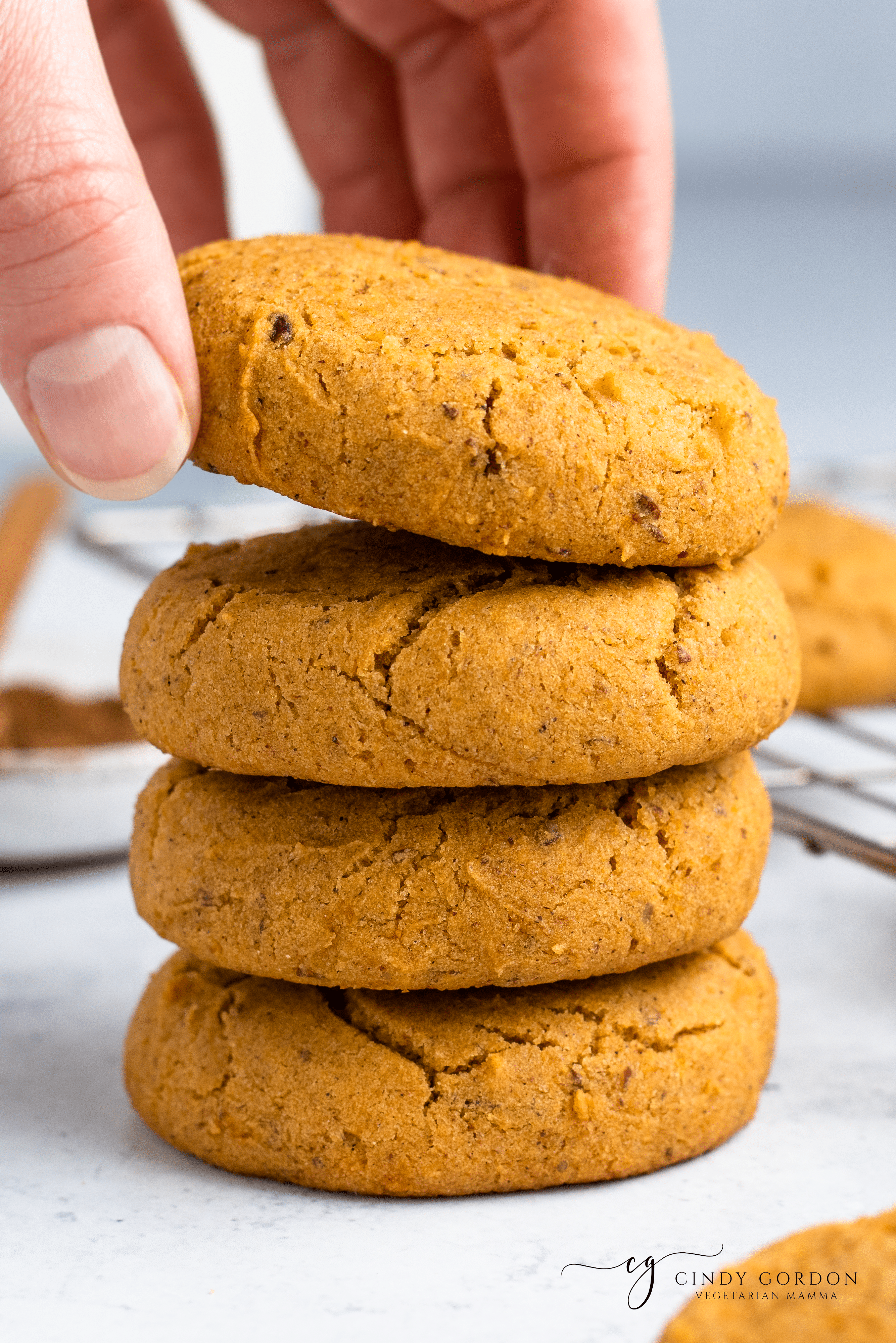 Someone picking up a cookie from the top of a stack of pumpkin cookies