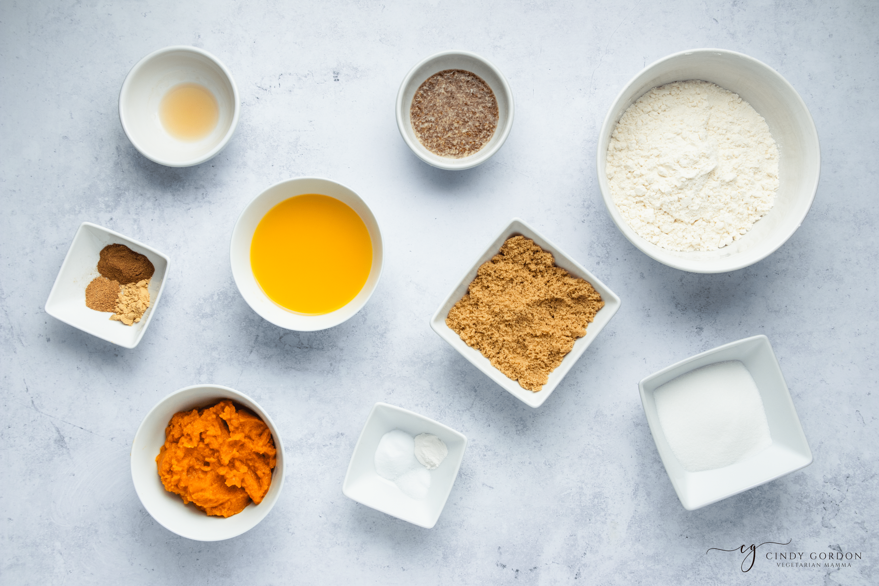 Bowls of gluten-free flour, brown sugar, pumpkin, spices, almond milk, and flax egg