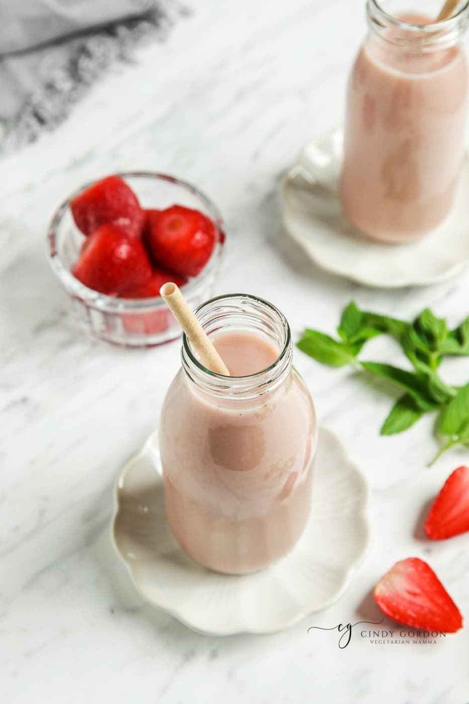 Overhead shot of creamy almond milk with strawberries in a glass bottle with a straw