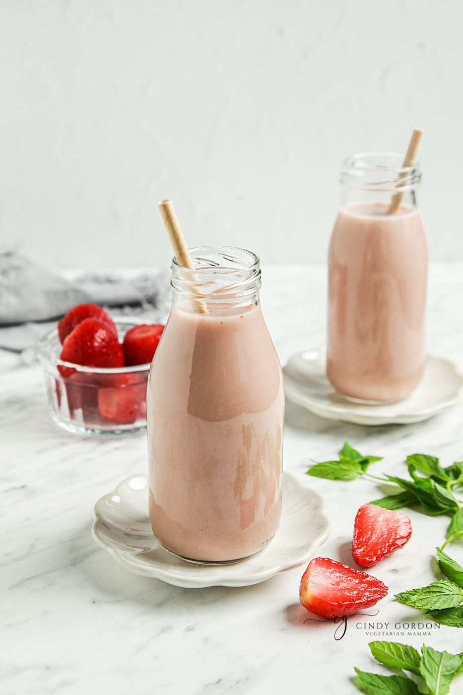 Two milk bottles of almond strawberry milk surrounded by milk and strawberries