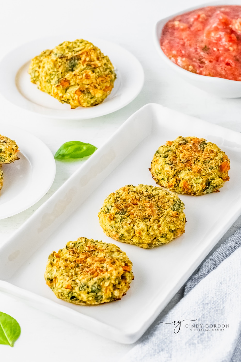 3 zucchini fritters on a white serving platter next to a bowl of salsa