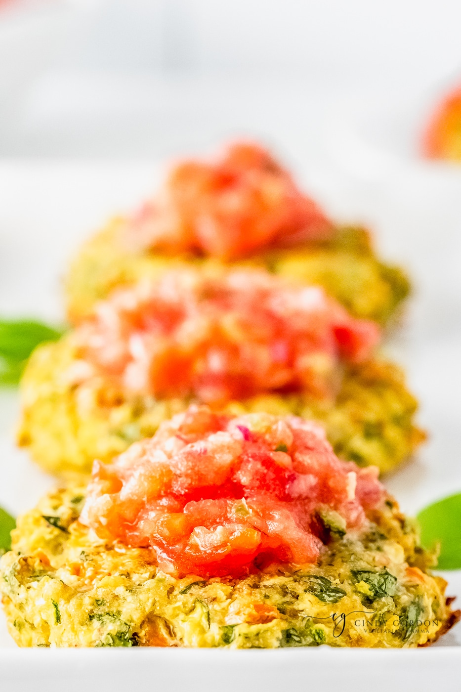Close-up shot of zucchini fritters topped with chunky tomato salsa on a white platter