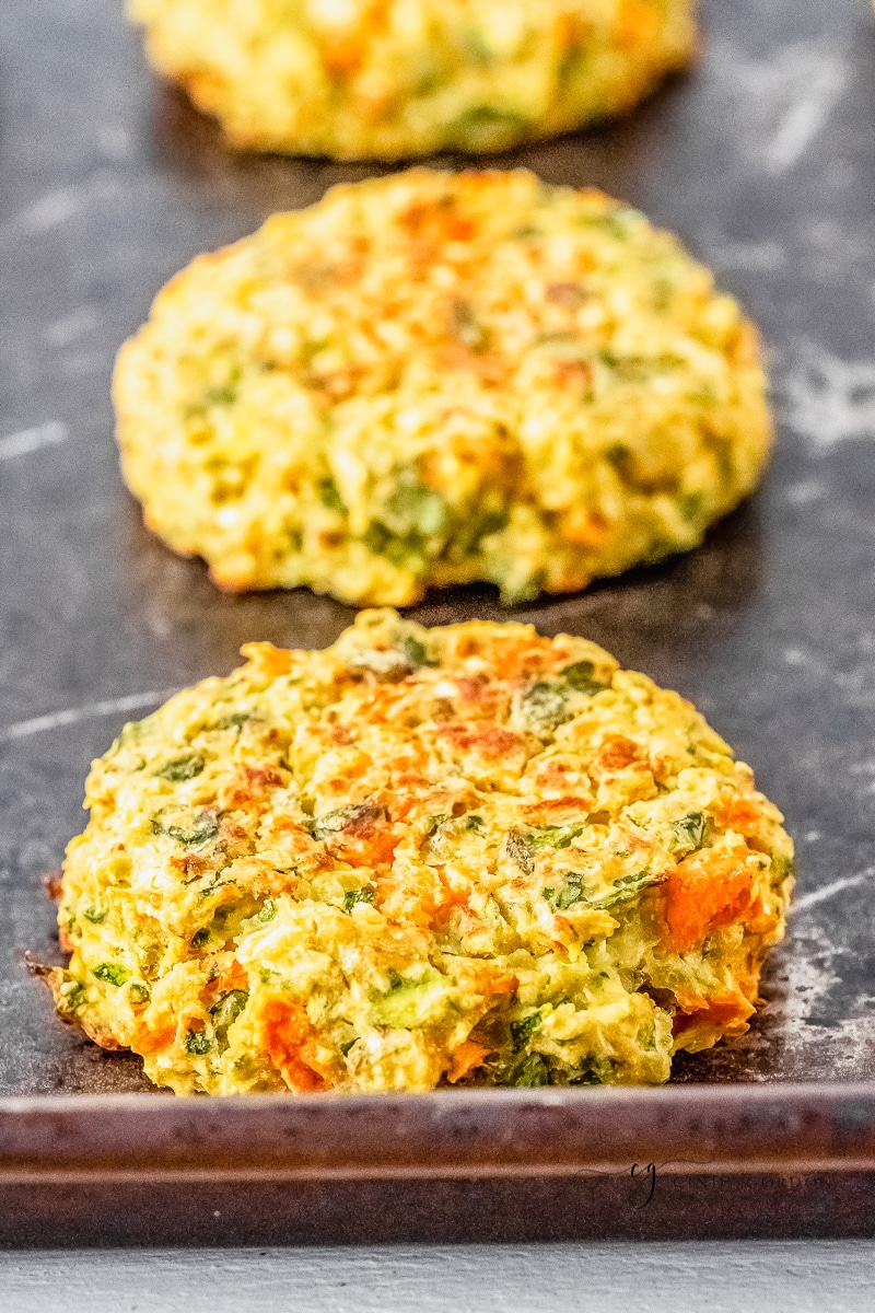 3 baked zucchini fritters on a baking sheet in a line