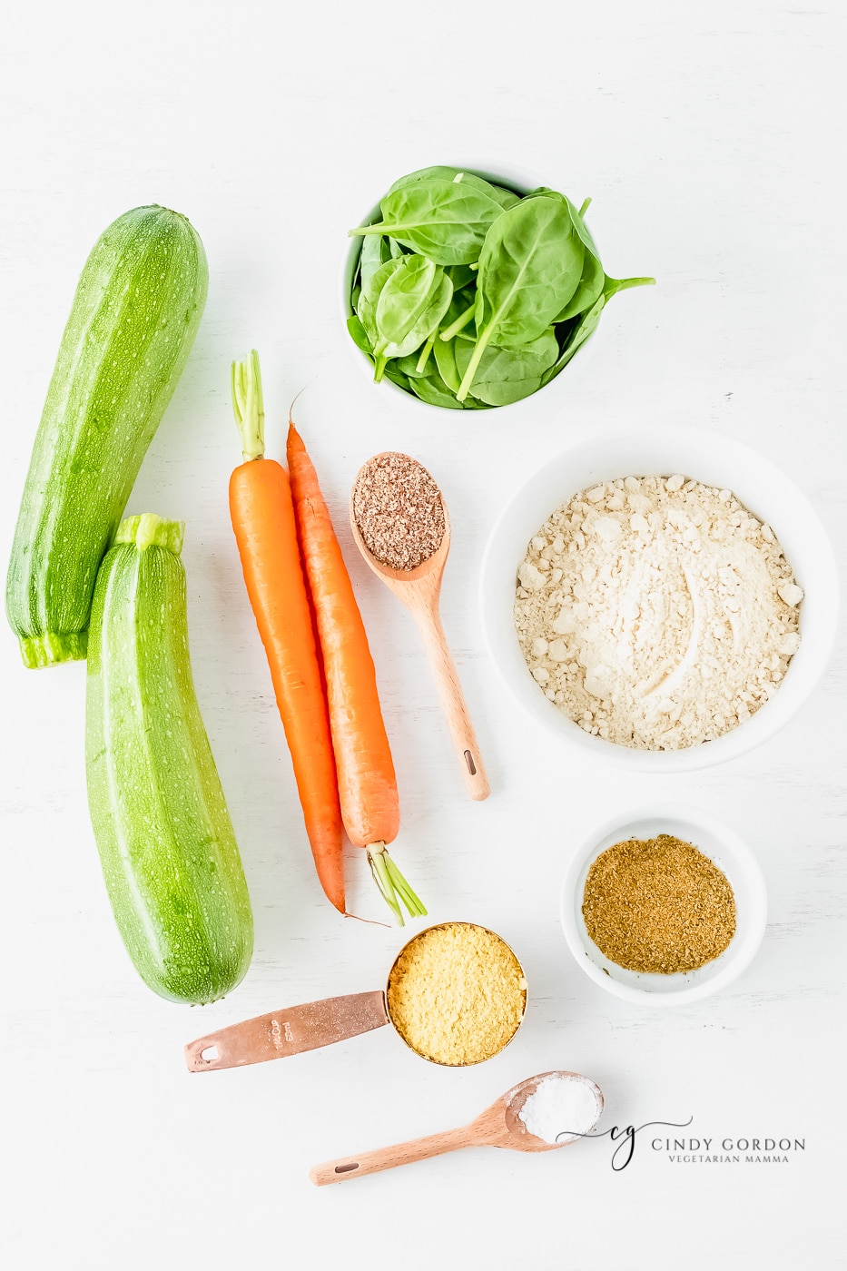 Zucchini and carrots next to bowls of spinach, nutritional yeast, chickpea flour, baking powder, and spices