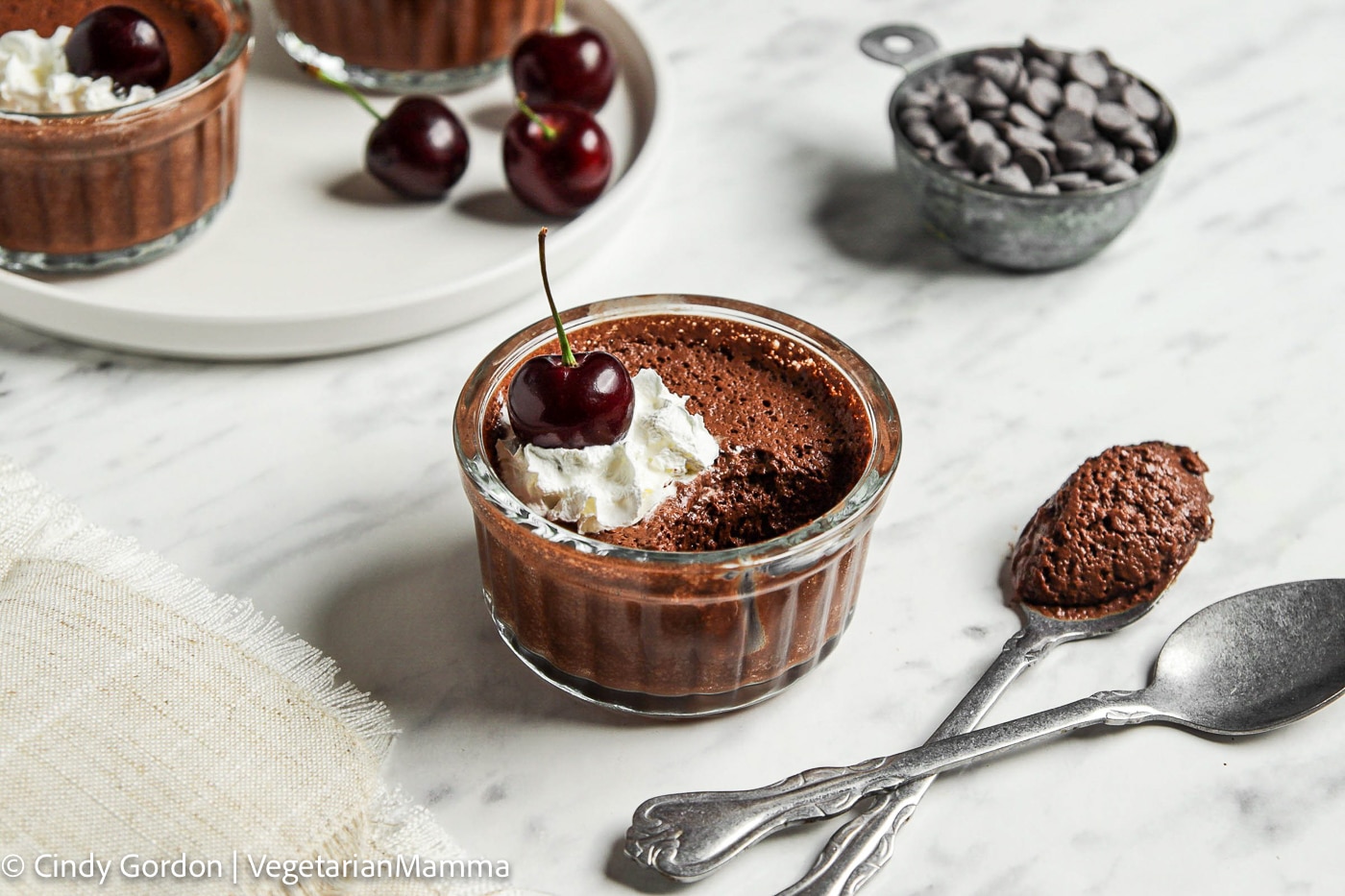 a ramekin filled with chocolate mousse with a bite taken out. Mousse is topped with whipped cream and a fresh cherry.