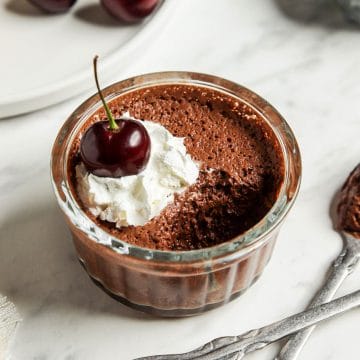 a clear ramekin filled with chocolate aquafaba mousse topped with whipped cream and a cherry.