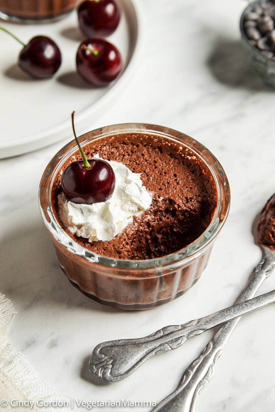 a clear ramekin  filled with chocolate aquafaba mousse topped with whipped cream and a cherry.