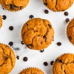 Vegan pumpkin chocolate chip muffins on a counter surrounded by chocolate chips