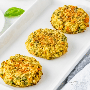 three baked zucchini fritters on a long rectangular white plate.