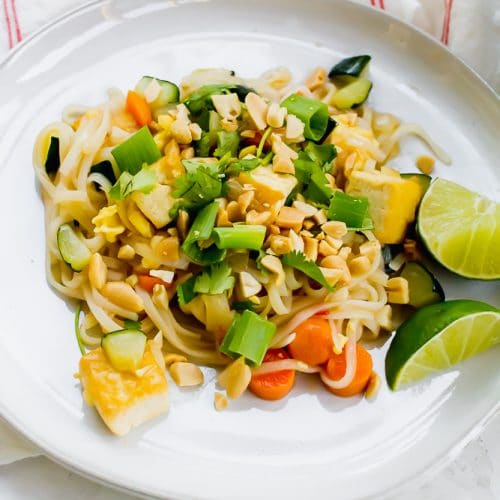 tofu, noodles, and vegetable pad thai on a white plate with lime wedges on the side
