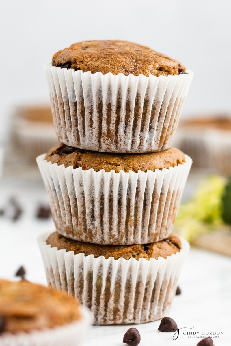 Close-up shot of a stack of 3 vegan zucchini muffins in white paper liners with chocolate chips