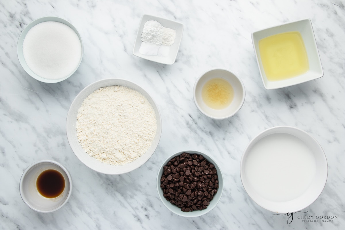 Bowls of flour, sugar, oil, vanilla extract, salt, and dark chocolate chips