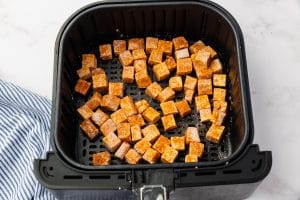 brown tofu chunks uncooked in black air fryer basket