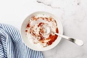 white and red powder mixed with a spoon in white bowl