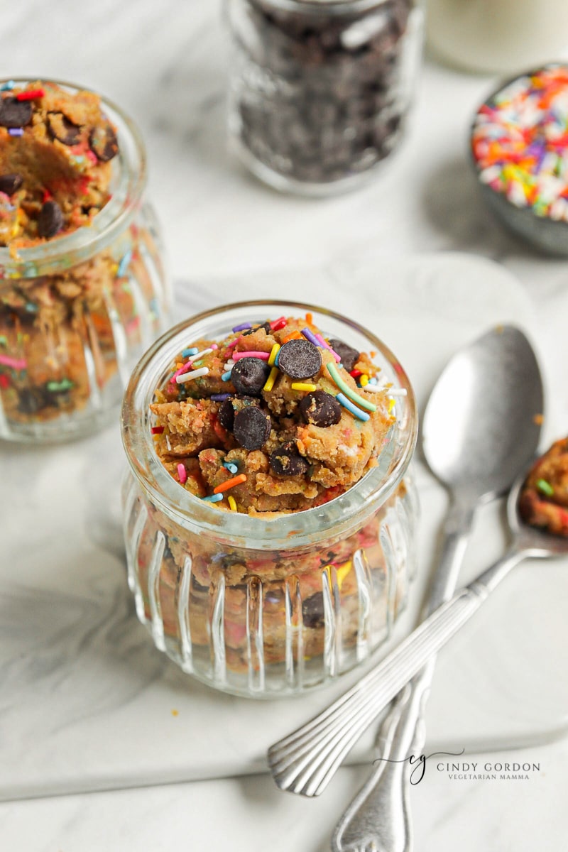 A glass jar full of vegan cookie dough topped with chocolate chips and sprinkles