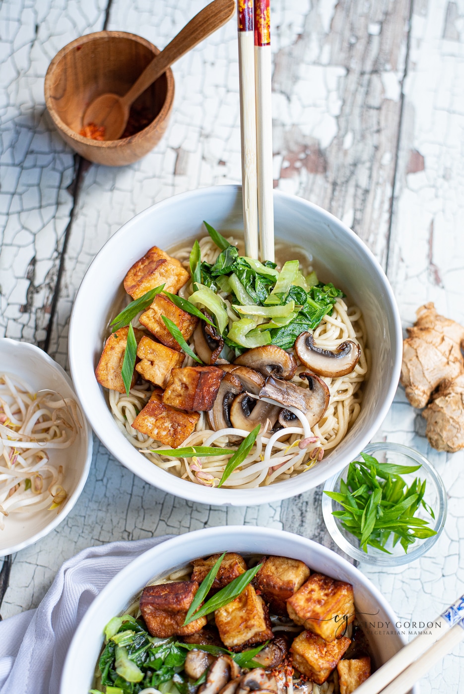 white ceramic bowl with noodles, mushrooms, greens and fried tofu with wooden chopsticks