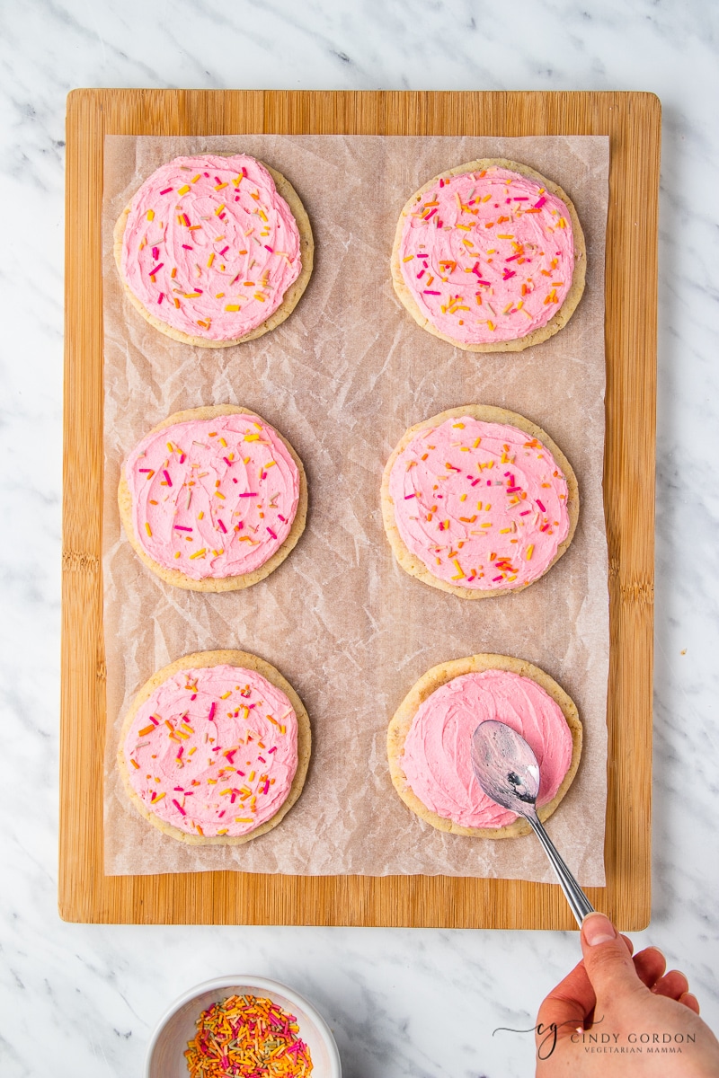 A hand frosting gluten free sugar cookies with the back of a spoon