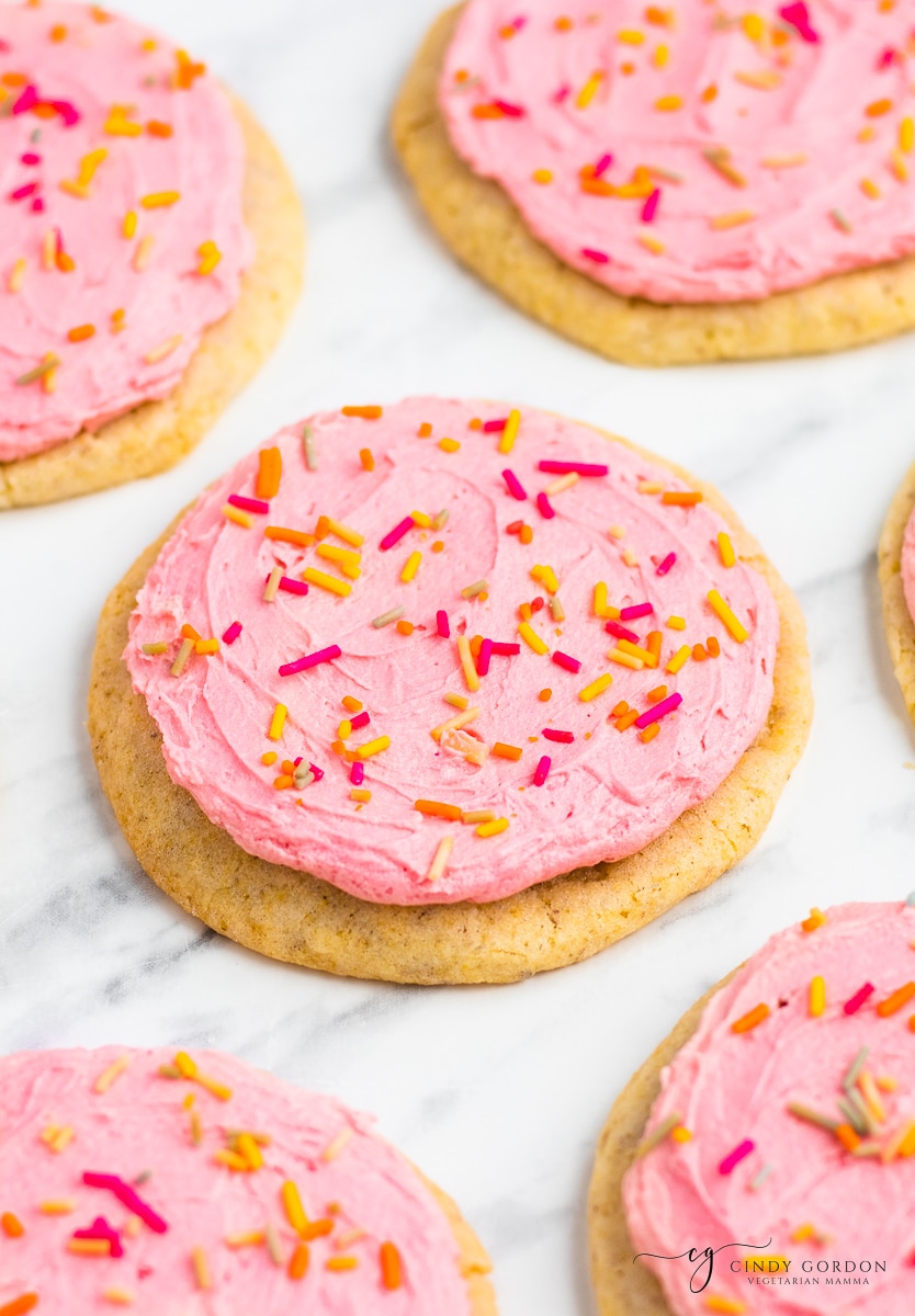 Vegan sugar cookies frosted with pink icing and covered with pink, yellow, and orange sprinkles