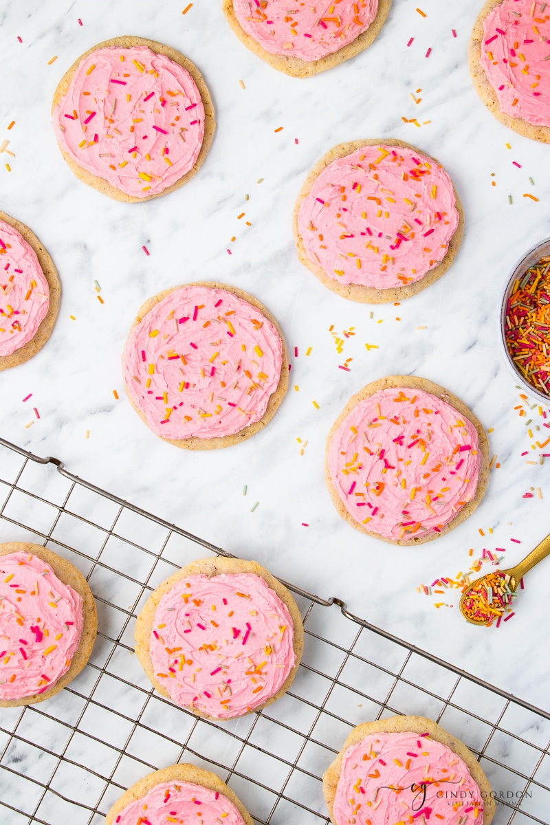 Pink frosted sugar cookies with sprinkles on a wire cooling rack and marble countertop