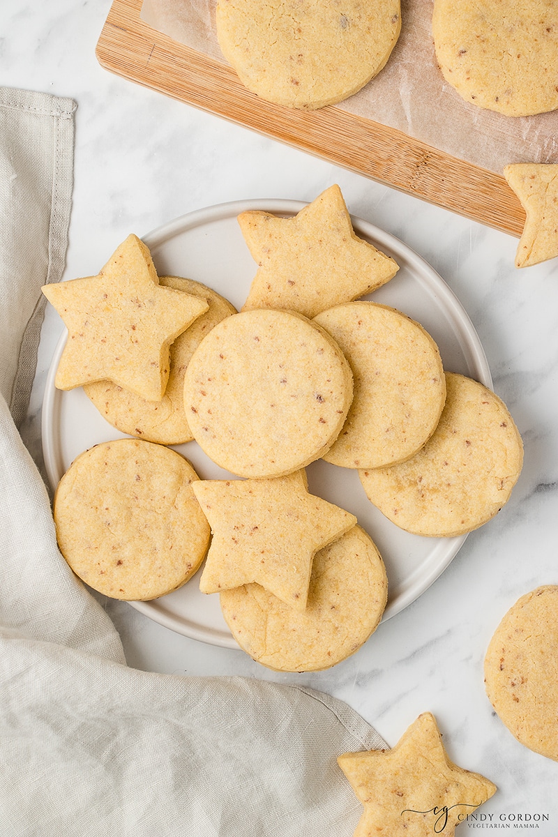 A white round plate of circle and star sugar cookies next to more cookies