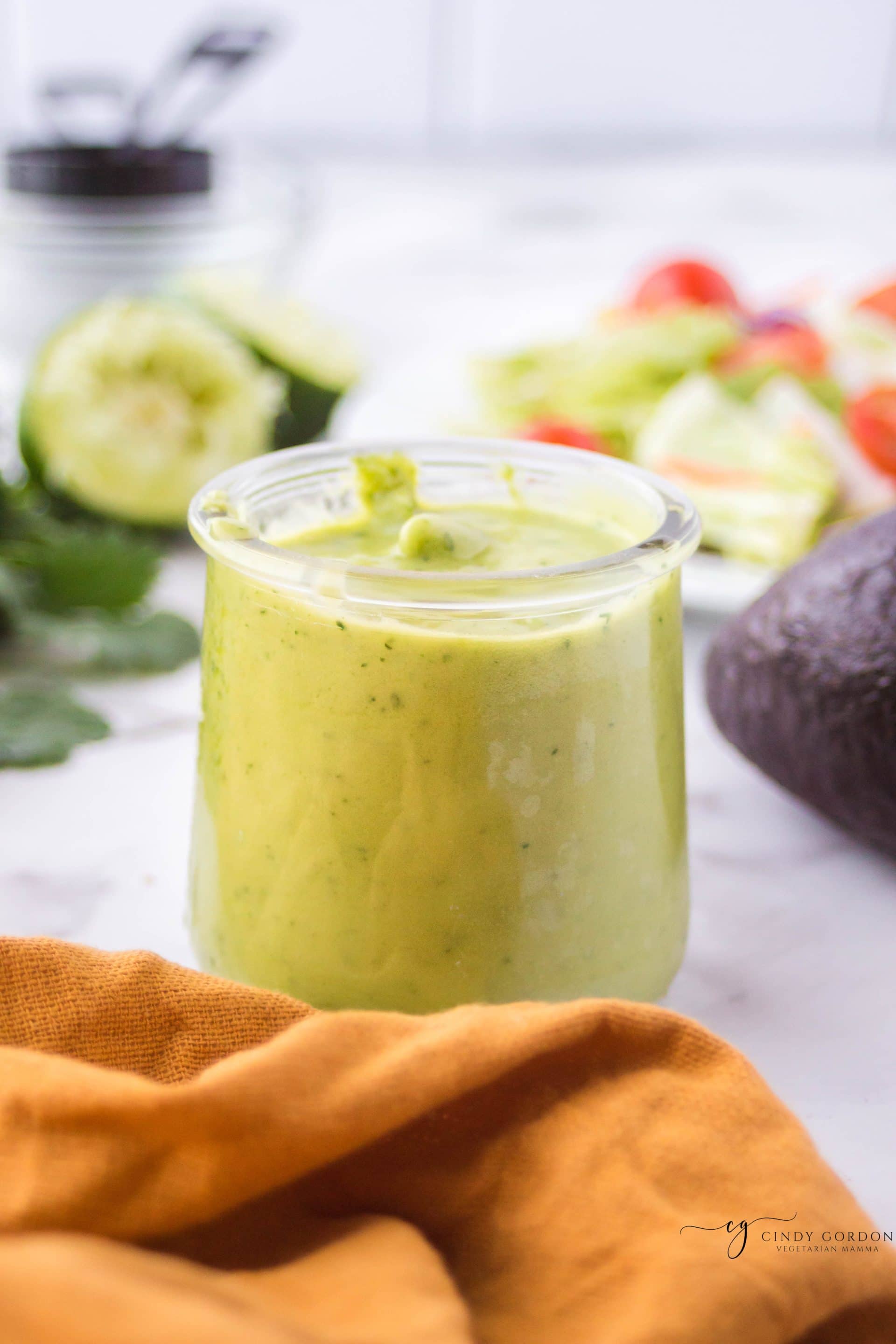 A jar of creamy avocado salad dressing with an orange towel in front
