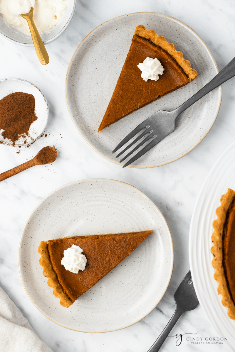 2 slices of sweet potato pie on round plates next to a bowl of cinnamon