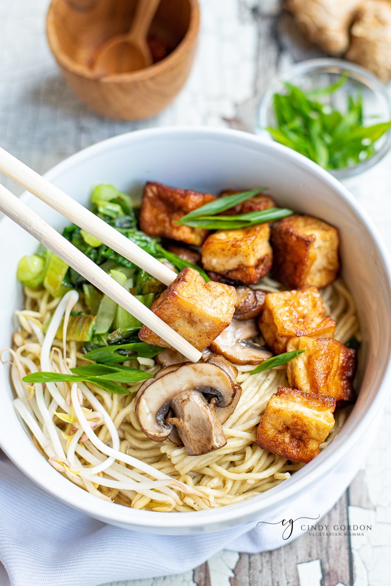 Chop sticks holding a crispy tofu cube over a bowl of soup