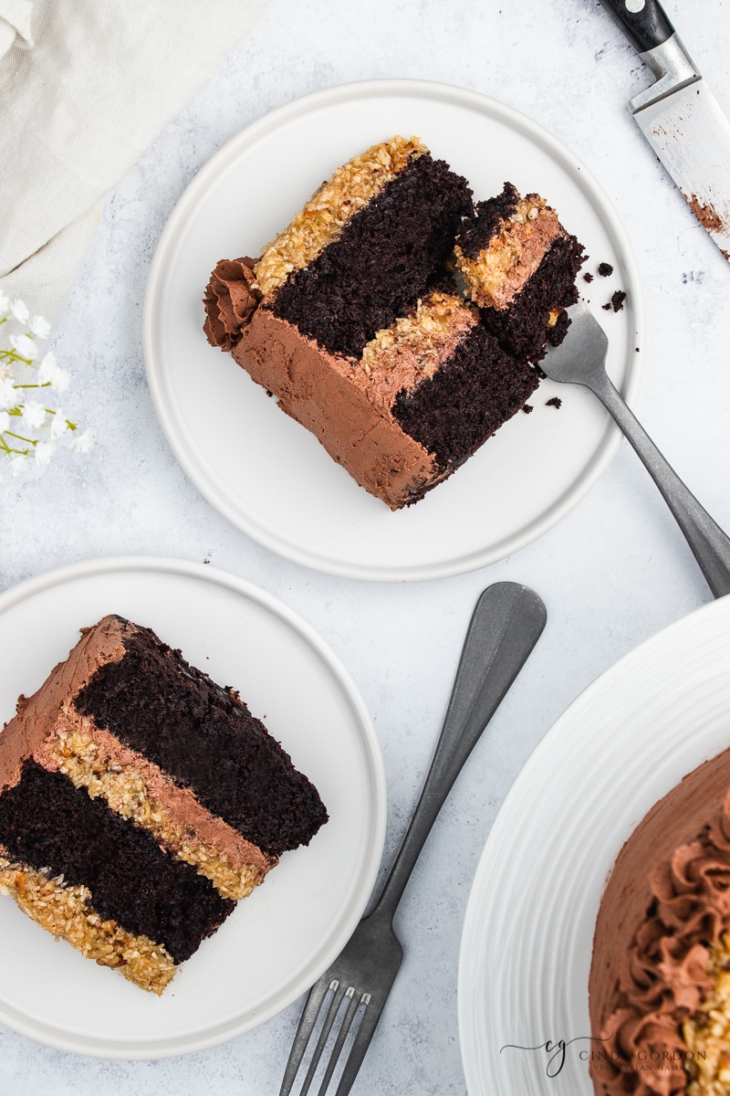 Two slices of German chocolate cake on round white plates with forks