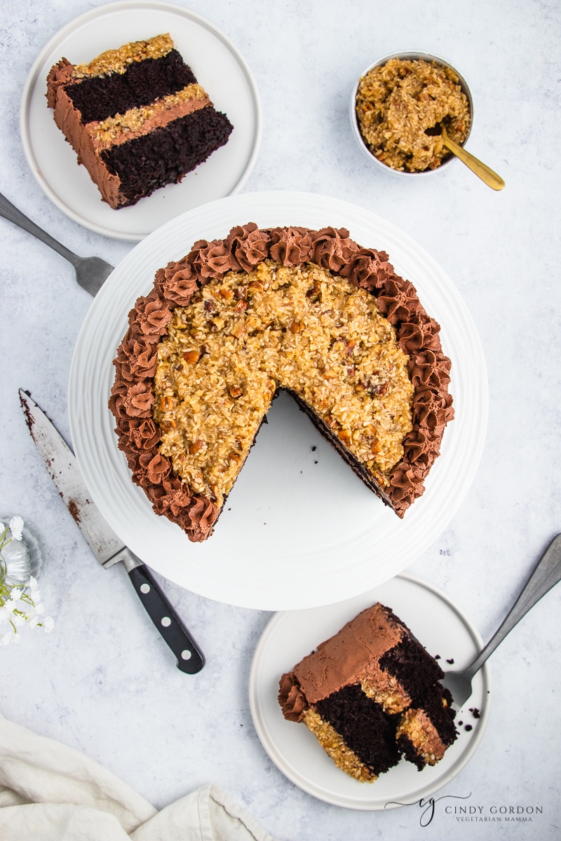 Two slices of vegan German chocolate cake on round plates next to a whole cake