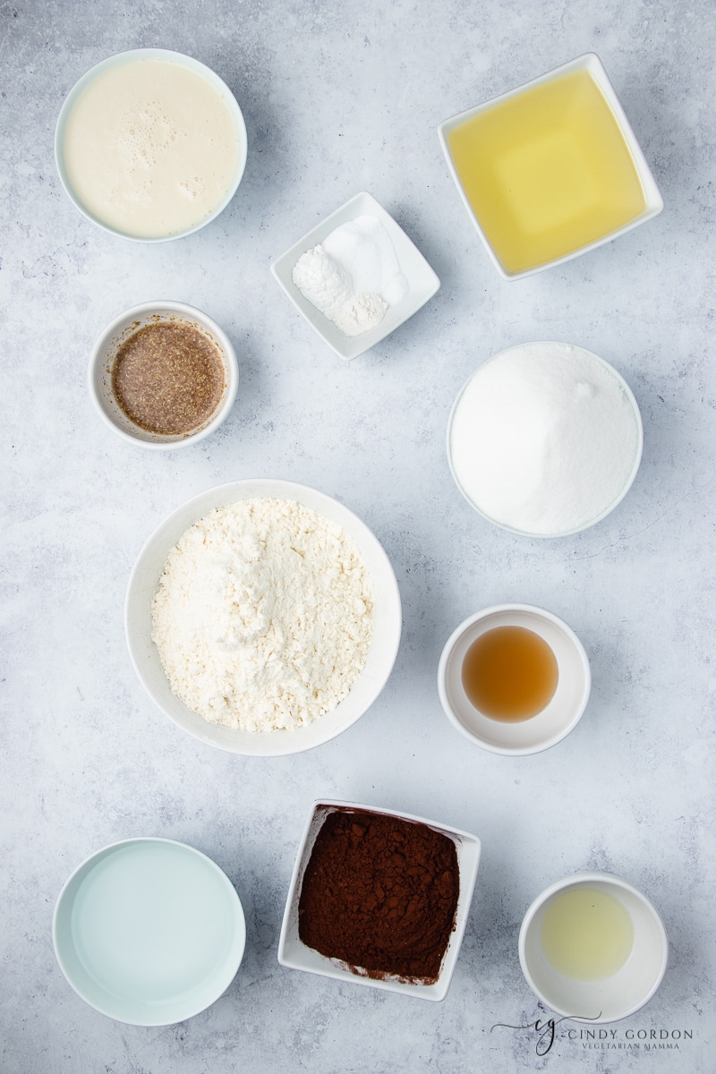 White bowls of gluten-free flour, cocoa powder, butter, sugar, oil, salt, flax egg, and cornstarch