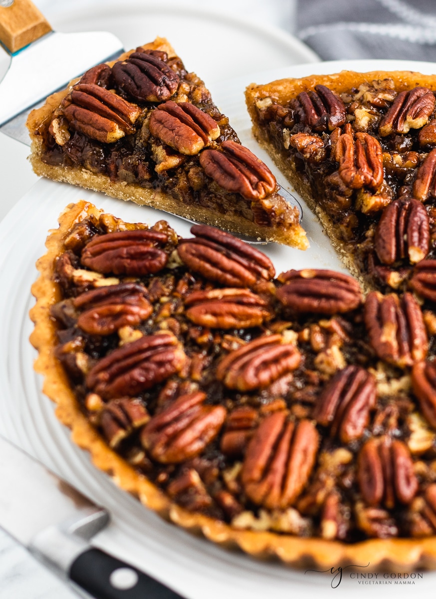 A spatula lifting a slice of pecan pie from a whole pie on a white plate