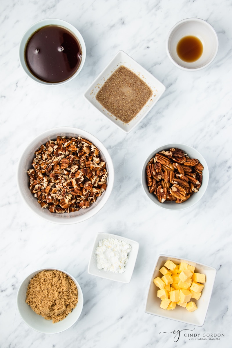 White bowls of pecans, flax eggs, vanilla extract, brown sugar, cornstarch, and butter