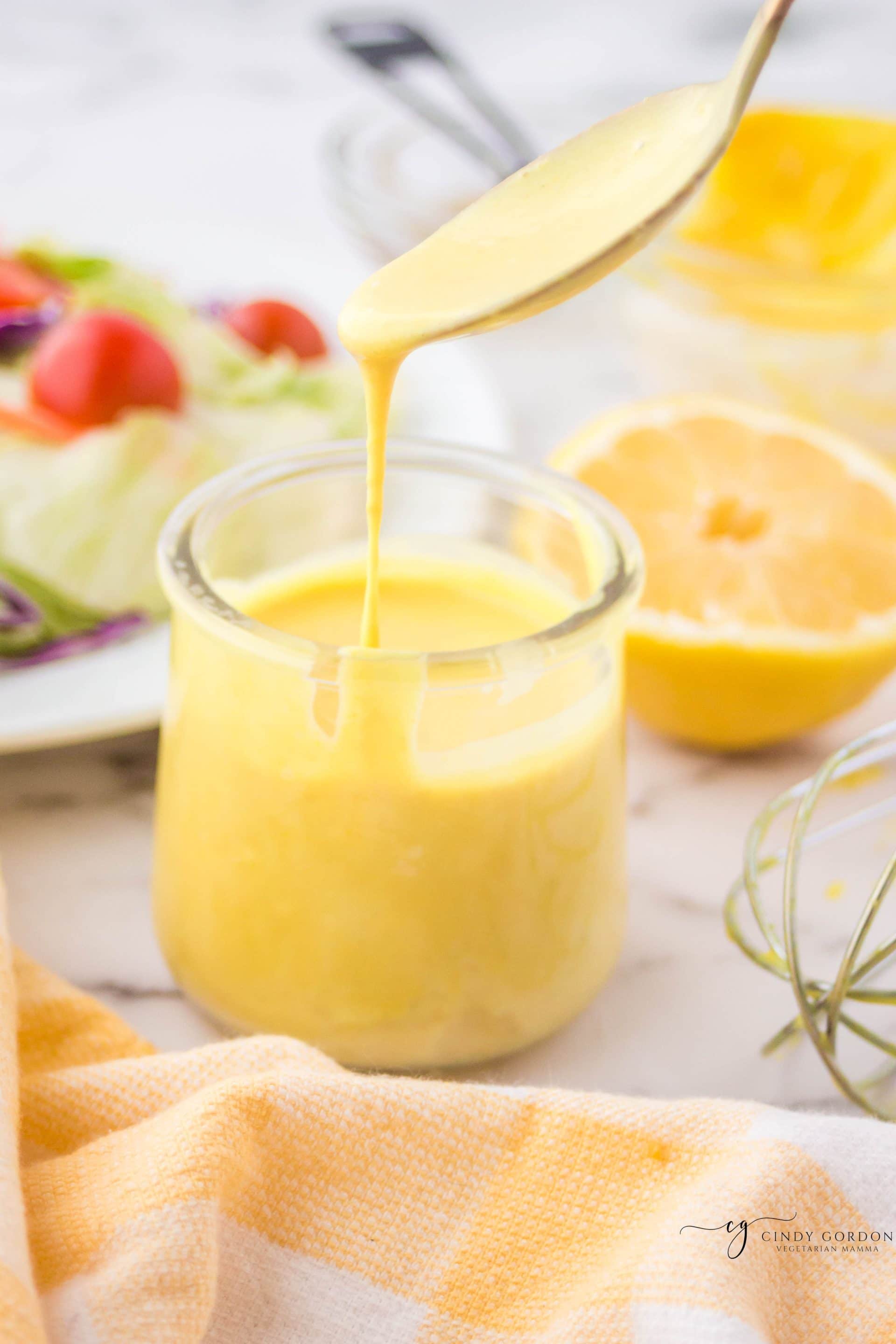 A spoon drizzling vegan honey mustard dressing into a small jar 
