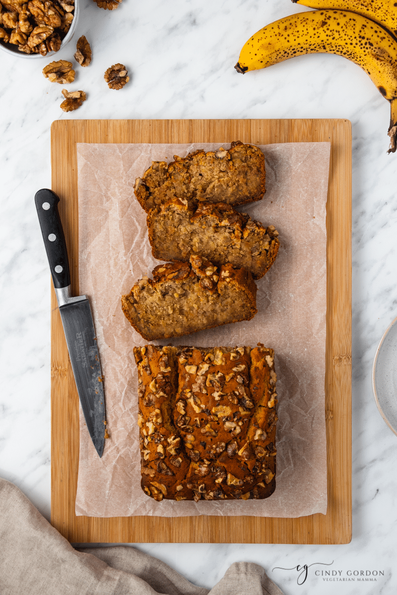 A half-sliced loaf of no sugar banana bread on a cutting board with a knife