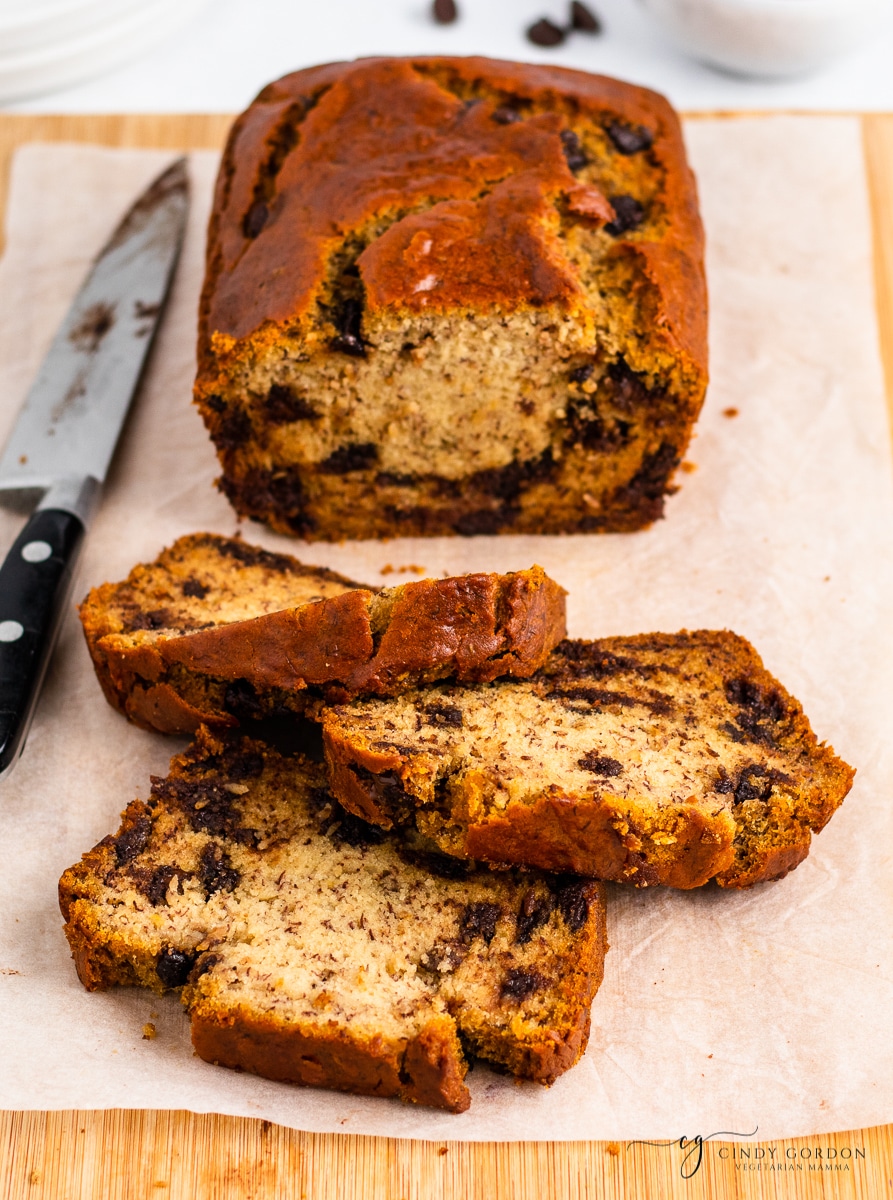 Slices of chocolate chip banana bread in front of a loaf on parchment paper