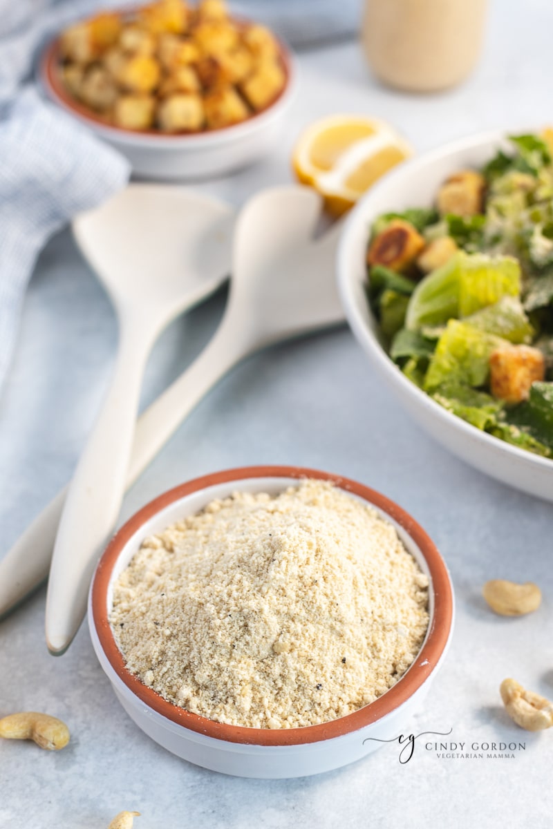 A white stone bowl of grated vegan Parmesan next to a salad bowl