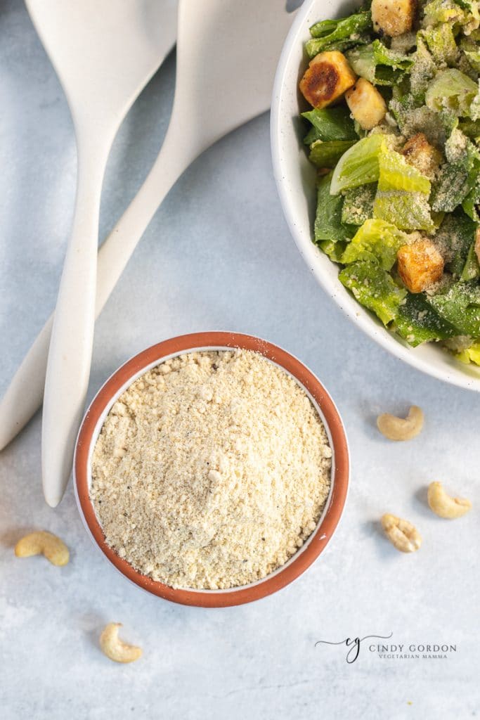 Overhead shot of a bowl of crumbled vegan Parmesan cheese with a Caesar salad