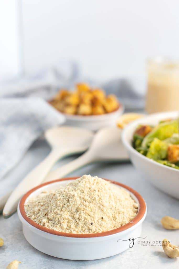 Vegan Parm in a white and orange bowl in front of croutons and a salad