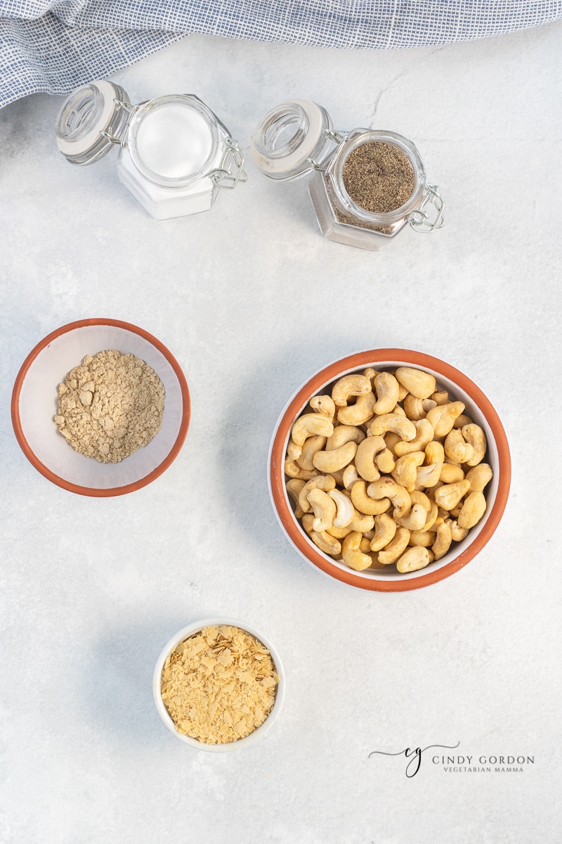 Bowls of cashews, nutritional yeast, salt, pepper, and garlic powder