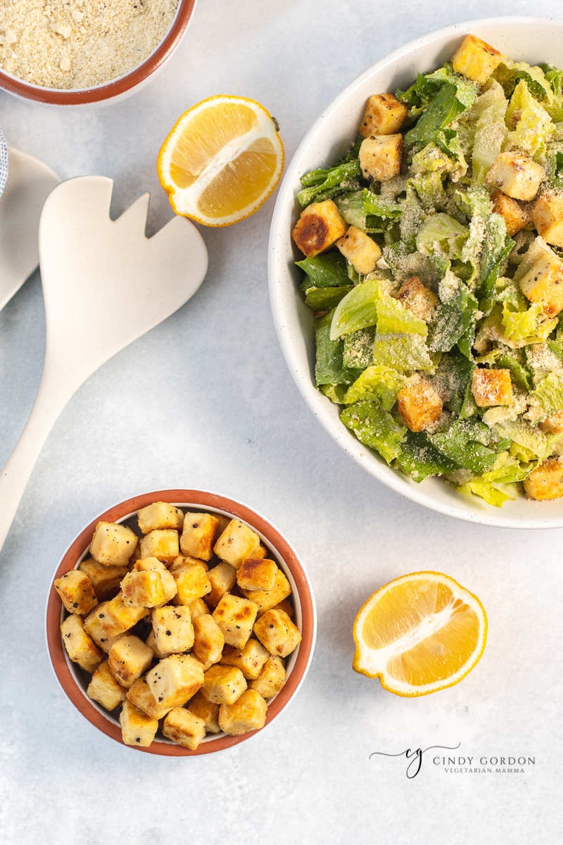 Overhead shot of a bowl of tofu croutons next to a large caesar salad