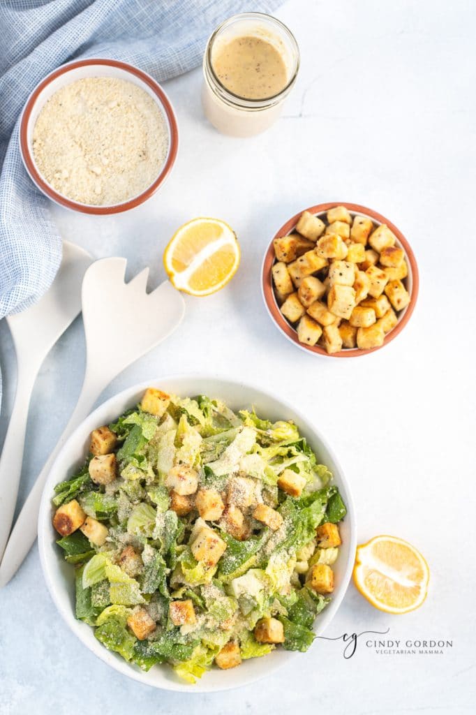 Overhead shot of bowls of vegan croutons, vegan Parmesan cheese, vegan Caesar dressing, and a salad