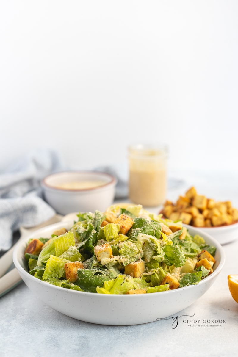 A salad dressed with vegan Caesar dressing with a jar of dressing and croutons