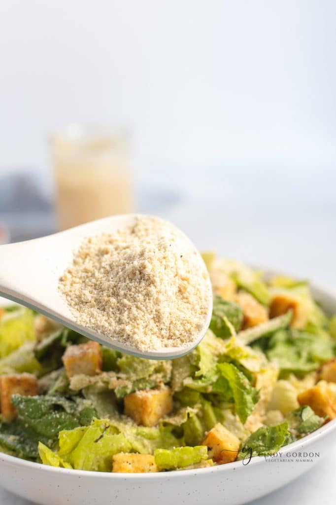 A spoonful of vegan Parmesan cheese over a crunchy Caesar salad