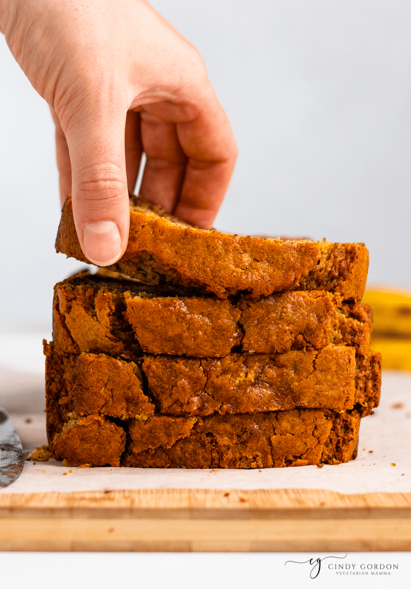 A hand picking up a slice of banana bread from the top of a stack