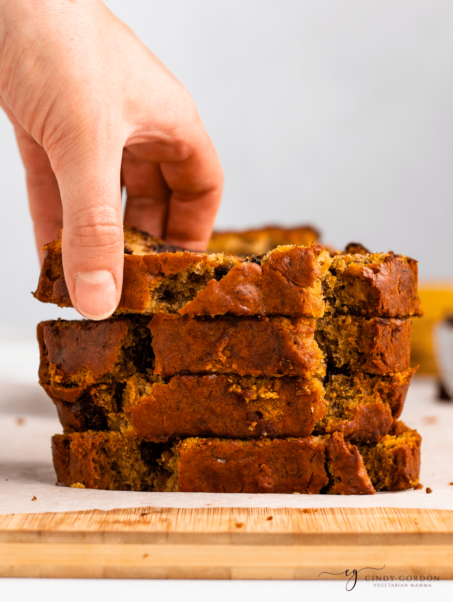 A hand taking a slice of banana bread off a tall stack of slices