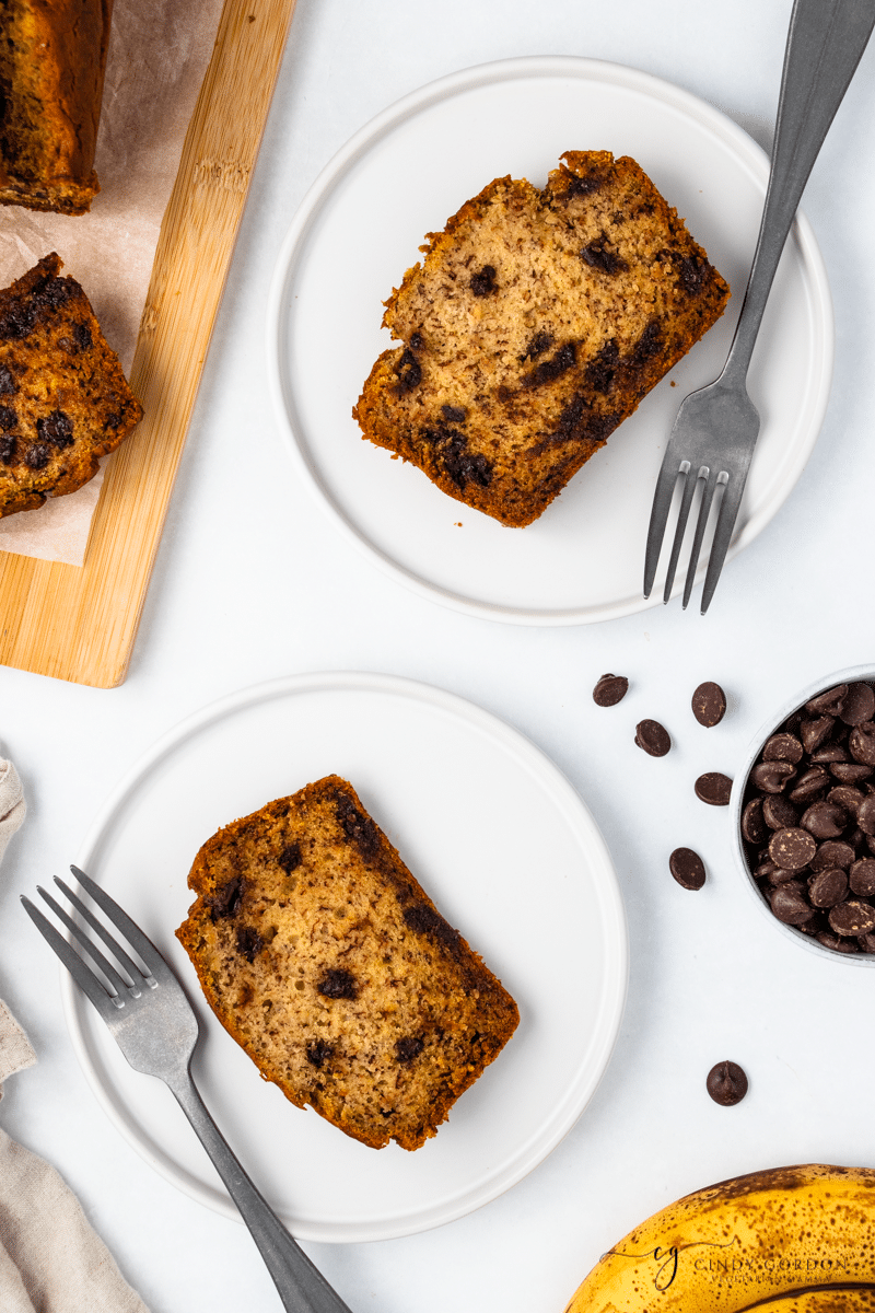 Two slices of vegan chocolate chip banana bread on white plates with forks